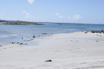 Sunny and relaxing beach with white sand at the coast of Brittany, with small boats and people fishing in the shallow water, pleasant mood, city at the opposite of the bay