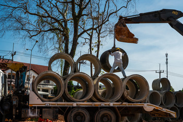 Using an excavator to translate large pipes into a vehicle helping a person.