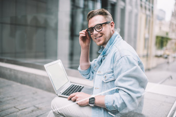 Joyful freelancer doing remote work using laptop in street