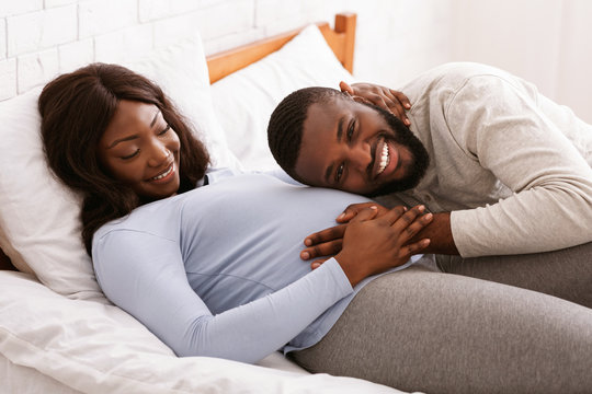 Excited man listening to his pregnant wife belly at home