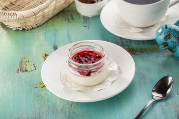 Dessert panna cotta with cherry jam and cup of black tea on blue wooden table