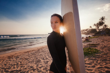 Beautiful young woman with dark hair with a surfboard in the sunset sunshine on the ocean