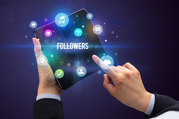 Businessman holding a foldable smartphone with FOLLOWERS inscription, social media concept