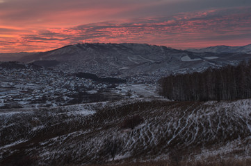 Winter dark sunset snow mountain slope on the background of village hills under colorful sunset sky