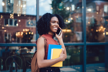 Contemporary black businesswoman in casual outfit speaking on smartphone at city street
