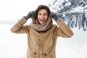 Handsome Man Pulling Scarf On Head Standing In Snowy Forest