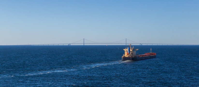 cargo ship in deep blue sea with Oresund brudge at horizon