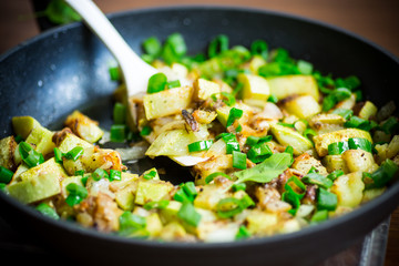 zucchini fried with onions and herbs in a pan on a wooden table
