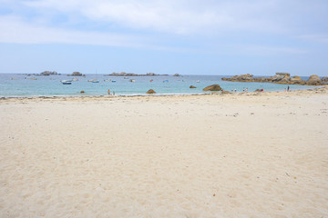 Beach with white sand, a few people and small boats in the water