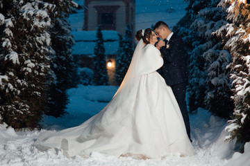 Winter wedding couple, bride and groom hugging in the snowy forest at their fairy wedding day. Wedding in winter, happy couple, bride and groom in the snowy forest in cold winter 