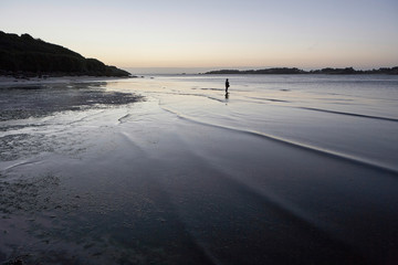 Lonely boy standing in the shallow water of a bay, dusk mood, loneliness