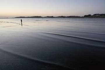 Low tide at a beach in Brittany in the evening, boy standing  alone in the shallow water, looking...
