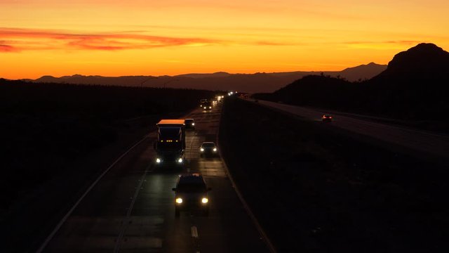 DRONE: Commuters and truckers drive down the famous Mojave freeway at scenic twilight. Picturesque golden evening sky gently illuminates the highway leading traffic across the rugged Mojave desert.