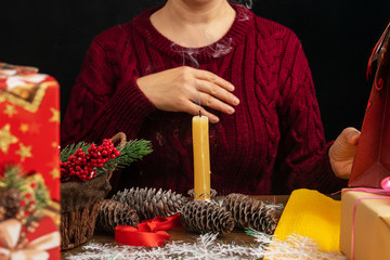 The candle is on the table. Around her are fir cones, Christmas gifts and Christmas decorations....