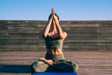 Concentrated young fit woman exercising meditation lotus on promenade
