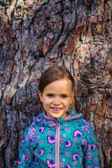 Little girl stands near giant old-growth  relic tree trunk in forest on sunny day. Nature care...