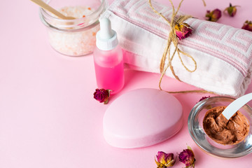 Rose flavored skin care cosmetics, soap, oil, face mask and bath salt on pink background with roses.