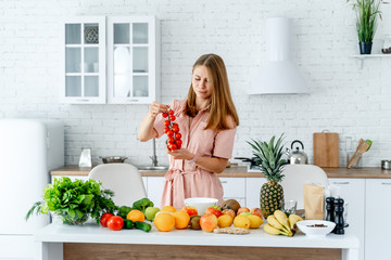 Pure, ripe juicy tomatoes in the woman's hands of a kitchen background. Table full of vegetables and fruits, modern kitchen
