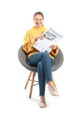 Young woman with newspaper sitting in armchair against white background