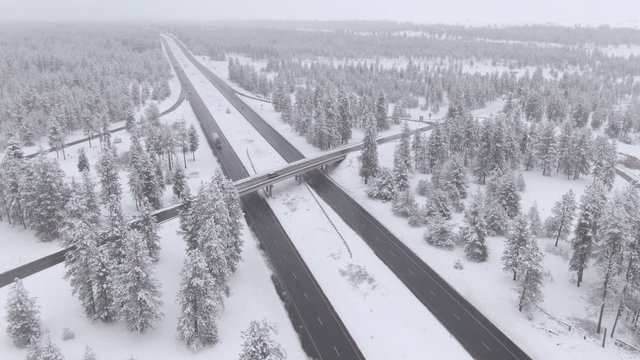 AERIAL: Scenic drone view of white snowy landscape surrounding a busy interstate highway in Washington, USA. Flying high above traffic driving along a slippery asphalt highway crossing the snowy woods