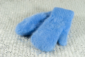 Fototapeta na wymiar Blue wool mittens on a bright shiny background