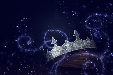 low key image of beautiful queen/king crown over old book and wooden table. vintage filtered....