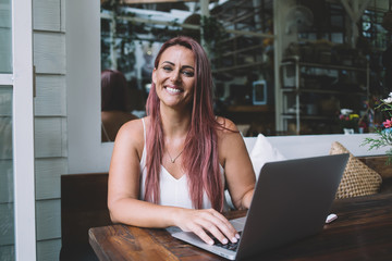 Positive female freelancer with laptop in restaurant