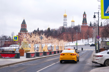 Moscow street near the Kremlin wall, tower and dome of the temple, yellow taxi on the road, trees...