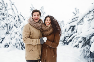 Fototapeta na wymiar Excited Couple Embracing Standing In Beautiful Snowy Forest