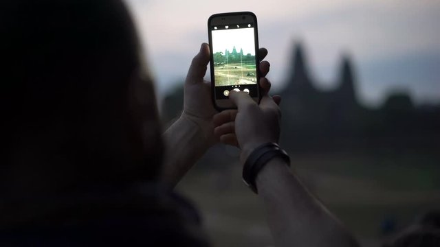 Man taking photos with smartphone of ancient Angkor Wat temple ruins in Cambodia