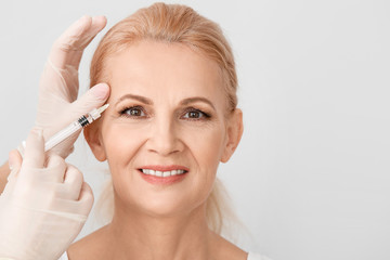 Mature woman receiving anti-aging injection in her face against light background