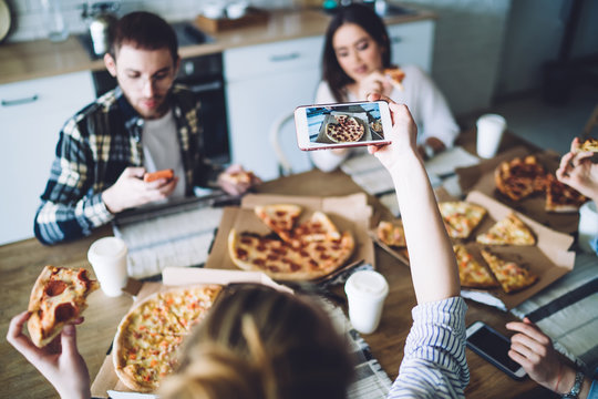 Unrecognizable woman taking photo of pizza during friends gathering