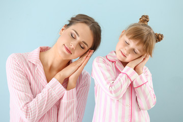 Portrait of sleepy mother and daughter in pajamas on color background