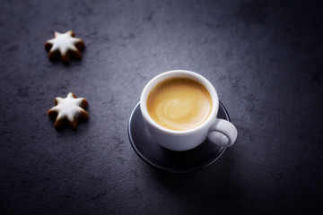Cup of coffee and Christmas cookies (cinnamon stars) on dark stone background. Copy space