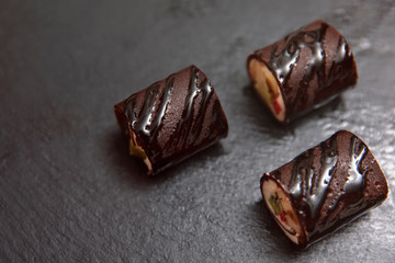 Photo of Chocolate Maki Sushi Pancake Rolls Stuffed with Fruits and Cheese Top View. Sliced Dessert with fruits and Sweet Brown Sauce on a black slate board