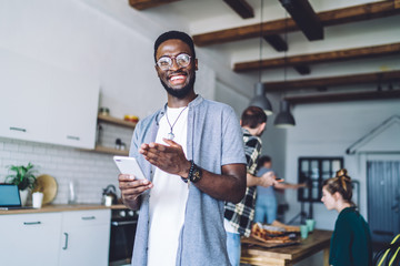 Confused smiled African American guy texting on smartphone at home