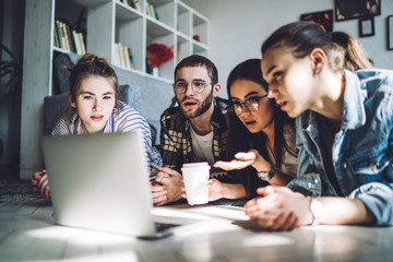 Shocked friends browsing laptop while relaxing on apartment floor