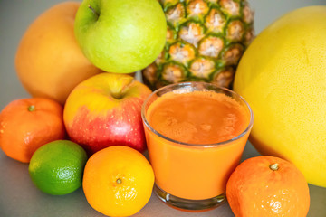 Different tropical fruits and orange smoothie on grey background, healthy eating lifestyle concept