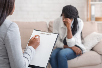 Female psychologist noting problems of young woman at psychotherapy session