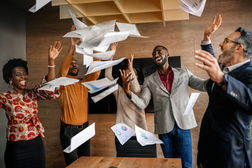 Diverse South African business team throwing papers in the air. Team celebrating a successful financial end of year - obrazy, fototapety, plakaty