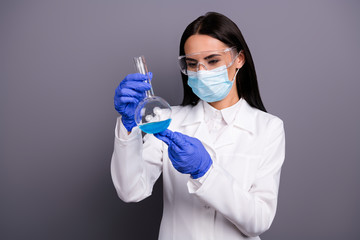 Portrait of concentrated scientist woman work in lab make new vaccine analyze chemical blue liquid hold flask wear white coat mask gloves goggles isolated over grey color background