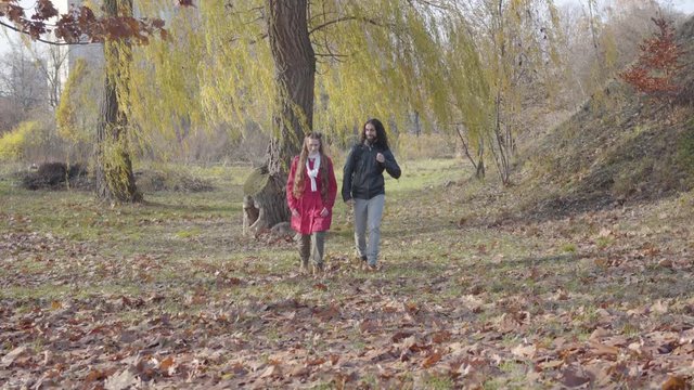 Joyful Middle Eastern boyfriend and Caucasian girlfriend strolling between trees in autumn forest. Carefree hippie couple dating outdoors. Piece, resting, leisure, togetherness.