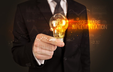 Businessman holding lightbulb with SOFTWARE IMPLEMENTATION inscription, Business technology concept