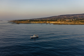 Aerial view of fishing boat in Mediterranean sea at background of Cyprus island. Beautiful nature landscape with water transport.