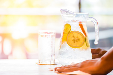 the fruit in the water and ice is on the table. the water in glass near jar. the hand and tissue paper clean the table.