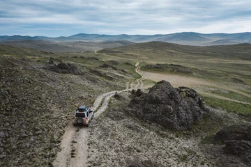 Sierkussen 4x4 suv auto rijden off-road pad op donker ruw terrein, luchtfoto. Reis in het landschap van steppeheuvels tussen rotsen en stenen. Olkhon Island, Siberië, Rusland © Vitaliy Kaplin