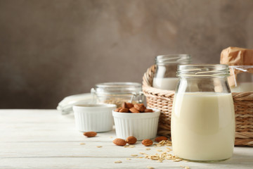 Bottle of oat milk, basket with a glasses of different types milk on wooden background, space for text