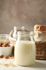 Bottle of oat milk, basket with a glasses of different types milk on wooden background, space for text