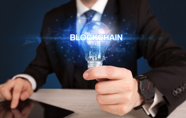 Businessman holding light bulb with BLOCKCHAIN inscription, innovative technology concept