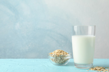 Glass of oat milk and oatmeal seeds on blue background, space for text